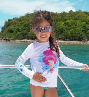 A small girl on a boat poses for the camera while wearing a sunshirt with a cartoon mermaid design